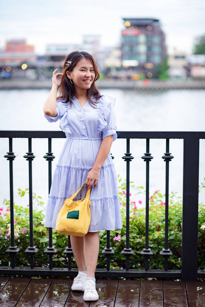 Портрет прекрасної азіатки в блакитній сукні з жовтим мішком для начиння на берегах річки.  - Фото, зображення