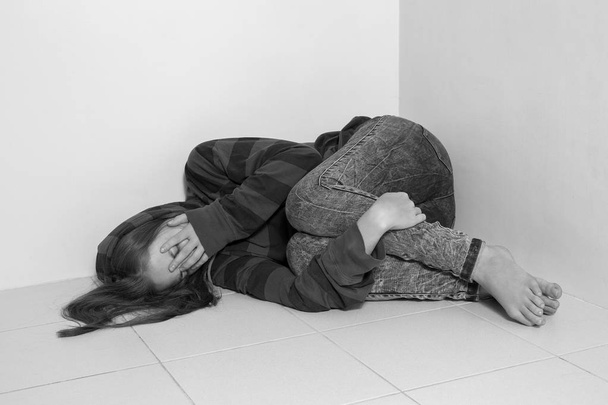 Νεαρή καυκάσια γυναίκα ξαπλωμένη στο πάτωμα, κλαίγοντας, αναστατωμένη, κακοποιημένη ή θλιμμένη. Μαύρο και άσπρο - Φωτογραφία, εικόνα