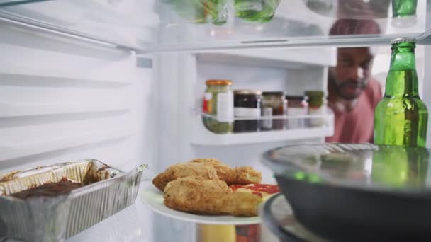 View from inside fridge as man opens door and takes out plate of unhealthy leftover takeaway fried chicken and pizza - shot in slow motion - Footage, Video