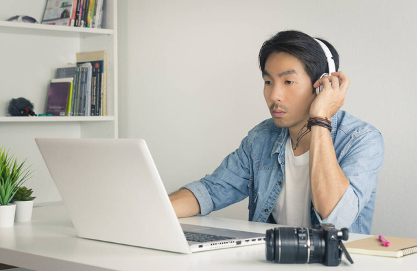 Videógrafo independiente asiático probando sonido multimedia por computadora portátil en su oficina en tono vintage
 - Foto, Imagen