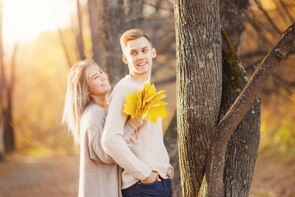 Liebendes Paar steht umarmt im Herbstwald in hellbeigen Pullovern, gelbem Hintergrund mit Blättern - Foto, Bild