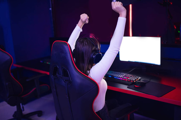 Стриптизерша-красавица радуется победе, играя в компьютерные онлайн-игры с наушниками, вид сзади
 - Фото, изображение