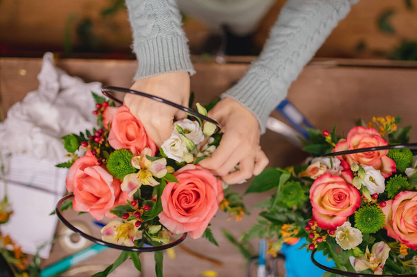 Ανθοπωλείο κορίτσι με τα χέρια της κάνει μπουκέτο λουλούδια σύνθεση από ροζ τριαντάφυλλα, φτέρη σε κουτί δώρου. Κάτοψη του χώρου εργασίας - Φωτογραφία, εικόνα