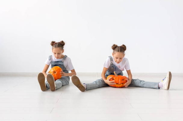 Boldog Halloweent, ünnepeket és gyermekkori koncepció - Aranyos ikrek nővérek lányok sütőtökkel Jack-o-lantern szórakozás közben időt otthon - Fotó, kép