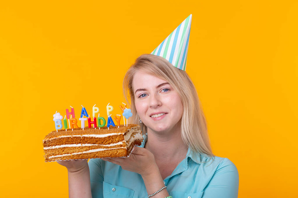 Svátky a večírek-pozitivní mladá žena, která má šťastný narozeninový dort na žlutém pozadí. - Fotografie, Obrázek