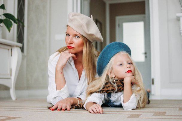 Young funny happy fair long hair mom and her cute girl dressed fashion family look having fun together lying on floor at living room, happy lifestyle - Zdjęcie, obraz