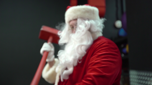 Santa Claus trénuje v tělocvičně na Štědrý den. Santa Claus nárazové kolo pneumatiky s kladivem. - Záběry, video