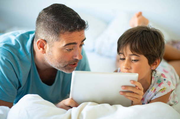 Батько середнього віку зі своєю восьмирічною дочкою, використовуючи цифровий планшет у спальні
. - Фото, зображення