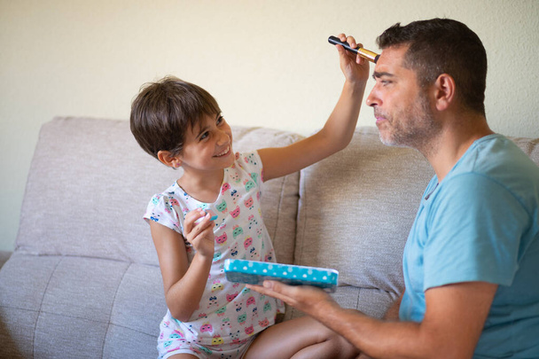 Mała śliczna córka robi makijaż do swojego ojca - Zdjęcie, obraz