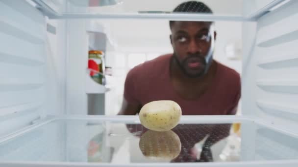 View from inside empty fridge as man opens door and picks up potato before closing door with disappointed expression - Video