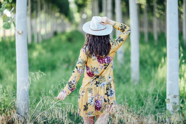 Genç kadın, çiçekli elbise giyiyor, ağaçların arasında. - Fotoğraf, Görsel