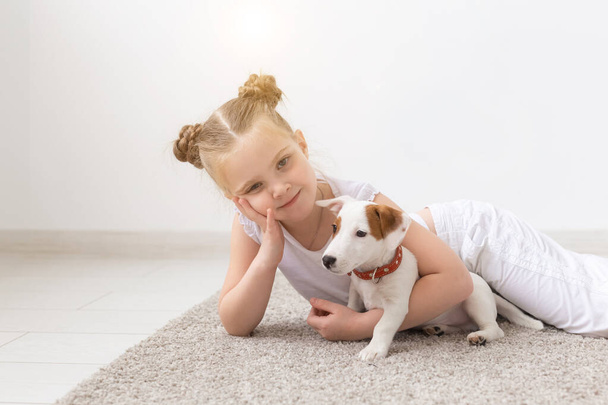 Mensen, huisdieren en dier concept - meisje zittend op de vloer over witte achtergrond en bedrijf pup Jack Russell Terrier - Foto, afbeelding