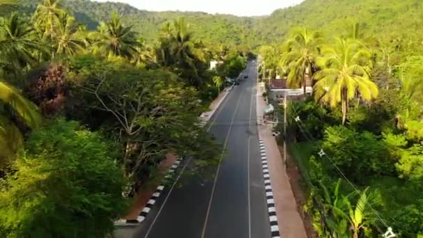 Aszfaltozott út a településen és a dzsungelen át. Aszfaltozott út megy keresztül kis tipikus település és zöld trópusi esőerdők Koh Samui paradicsomi sziget. Hegyek a láthatáron. Falusi élet - Felvétel, videó
