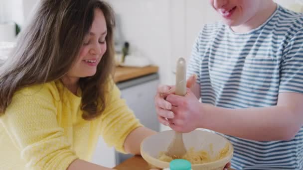 Young Downs Syndrome couple in kitchen at home mixing ingredients in bowl for cake recipe together - shot in slow motion - Materiał filmowy, wideo
