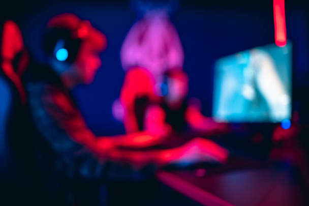 Fondo borroso jugador profesional jugando torneos juegos en línea ordenador con auriculares, rojo y azul - Foto, Imagen