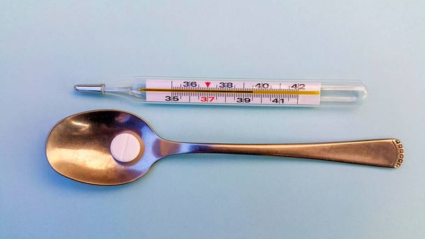 on a light blue background, a thermometer showing a high temperature and a spoon with a tablet, copy space for text. - Photo, Image