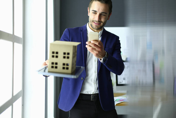 Businessman holding house miniature on hand standing in office. - Photo, image