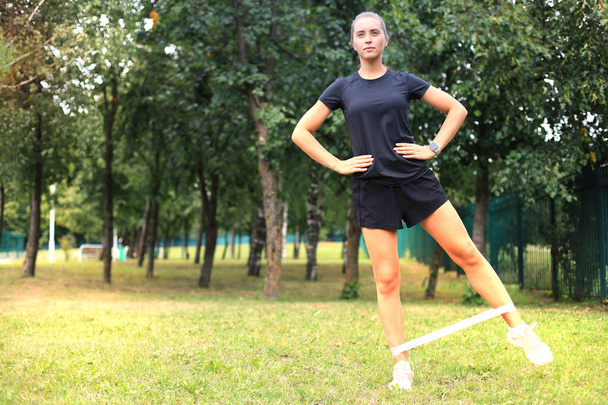 Fitness woman doing leg exercises with fitness gum in park. - Zdjęcie, obraz