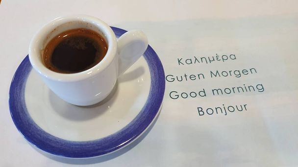 Una taza pequeña con café negro. A su lado, las palabras Buenos días en cuatro idiomas
. - Foto, imagen
