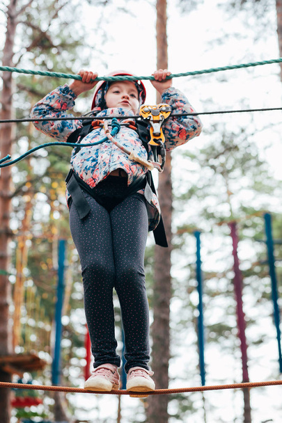 Retrato de una linda niña de 7 años que camina en una ciudad de cuerda (puente) en un parque de cuerda de aventura. ? ocio de hildren y juegos al aire libre
 - Foto, Imagen