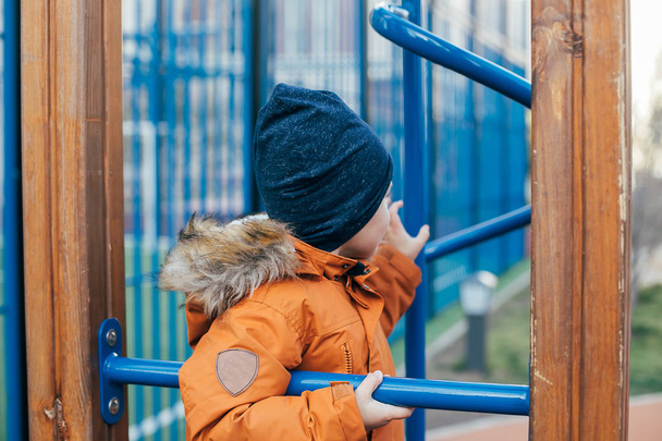 Egy 5 éves kisfiú narancssárga dzsekiben a játszótéren. Szabadidő a szabadban, játékok az utcán. - Fotó, kép