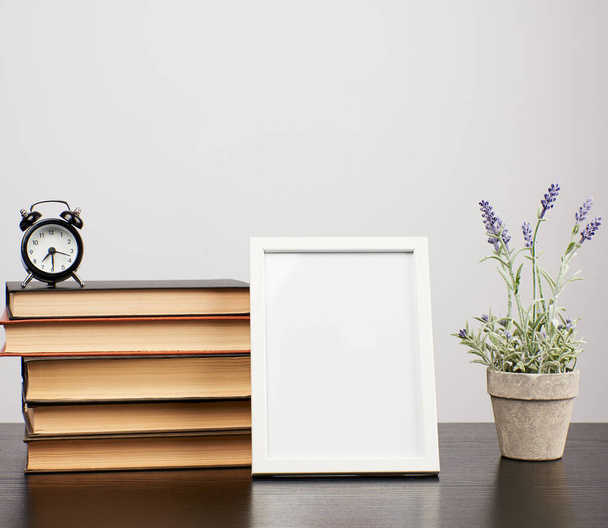 Leerer weißer Fotorahmen, ein Stapel Bücher und ein Topf mit wachsendem Lavendel - Foto, Bild