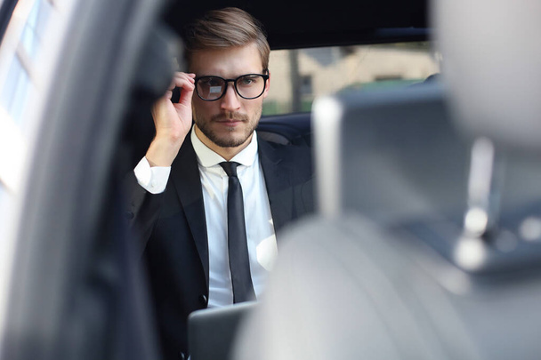 Thoughtful confident businessman keeping hand on glasses while sitting in the luxe car. - Foto, Imagem