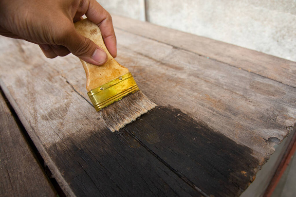 χέρι κρατώντας μια βούρτσα Ζωγραφική ξύλινη επιφάνεια σανίδων ξύλου με  - Φωτογραφία, εικόνα