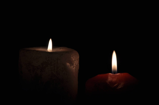 Dos grandes velas arden en la oscuridad. Sobre un fondo negro
 - Foto, imagen