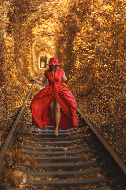 Όμορφη γυναίκα με κόκκινο φθινοπωρινό φόρεμα περπατά στο τούνελ της αγάπης. - Φωτογραφία, εικόνα