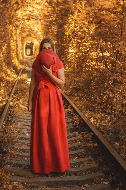 Όμορφη γυναίκα με κόκκινο φθινοπωρινό φόρεμα περπατά στο τούνελ της αγάπης. - Φωτογραφία, εικόνα