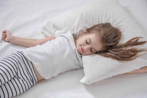 Cute little girl with long hair sleeping in bed. - Фото, изображение