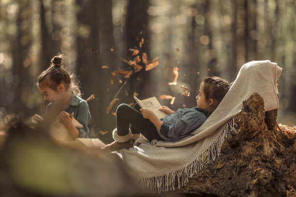 дві маленькі дівчата читають книги в лісі
. - Фото, зображення