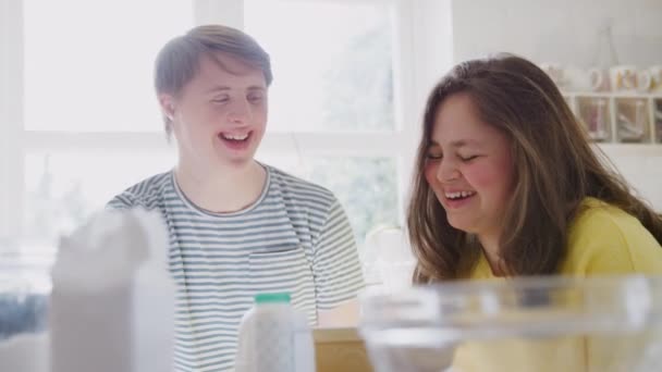 Young Downs Syndrome couple having fun laughing in kitchen at home baking cake together - shot in slow motion - Imágenes, Vídeo