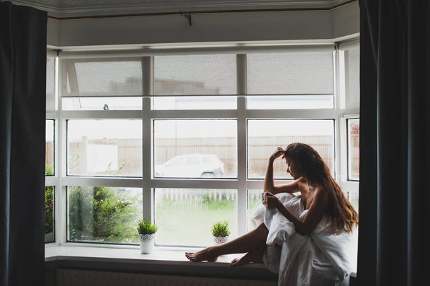 Yung nainen peitetty huopa istuu ikkunalaudalla ja enjoyi
 - Valokuva, kuva