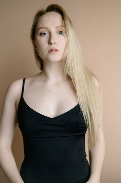 Graceful young woman in a black top posing against beige wall. - Foto, afbeelding