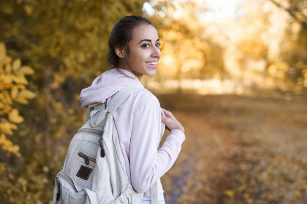 Autumn woman turns around at camera with charming smile, walking in autumn park with colorful leaves on fall nature background. - Valokuva, kuva
