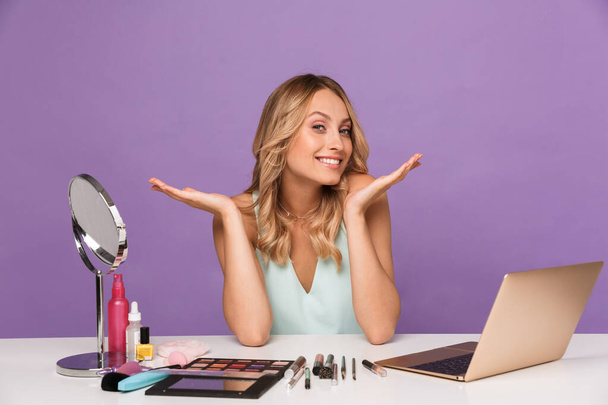 Image of smiling young woman using laptop while doing makeup - Fotó, kép