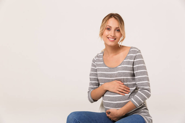 Image of smiling woman looking at camera and touching her belly - Photo, Image