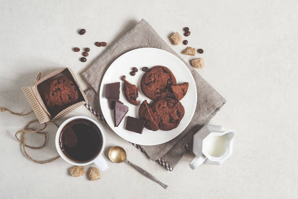 Oatmeal cookies with cocoa and chocolate on a white plate and in a cardboard box, cup of coffee and a milk jug - Foto, imagen