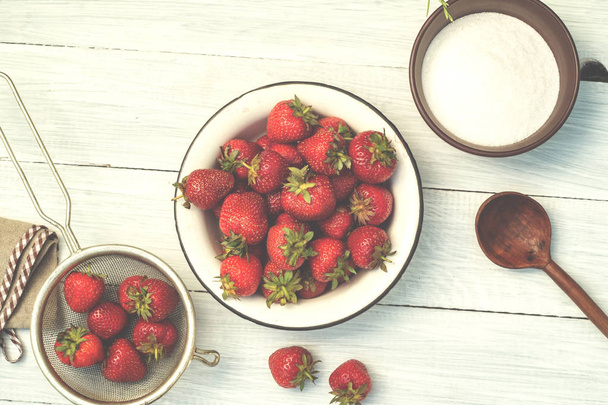 Ripe strawberries in a bowl, colander and sugar on a white woode - Foto, afbeelding