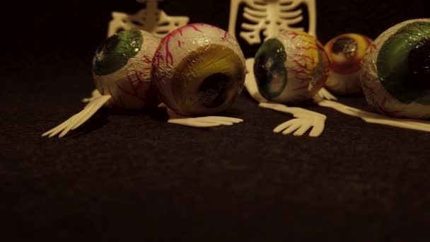 Middelen voor een Halloween feest met griezelige en angstaanjagende decoratie elementen zoals een Jack O 'Lantern, skeletten, en snoepjes in de vorm van oogballen in een stevige zwarte achtergrond. - Video