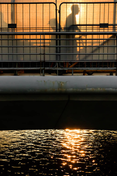 Silhouet van een man die over een brug loopt bij zonsondergang - Foto, afbeelding