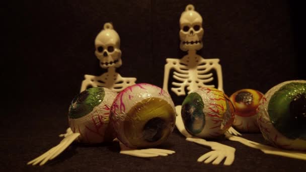 Middelen voor een Halloween feest met griezelige en angstaanjagende decoratie elementen zoals een Jack O 'Lantern, skeletten, en snoepjes in de vorm van oogballen in een stevige zwarte achtergrond. - Video