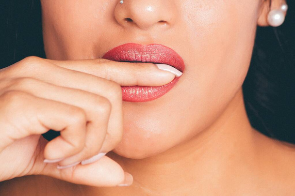 A closeup shot of a female wearing red lipstick biting her finger- great for an article about cosmetics - Foto, afbeelding