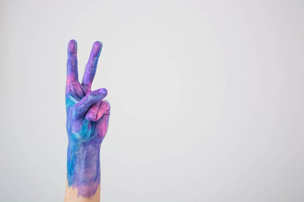 Blue and pink colored painted hand gesturing peace sign on a gray background - Фото, зображення