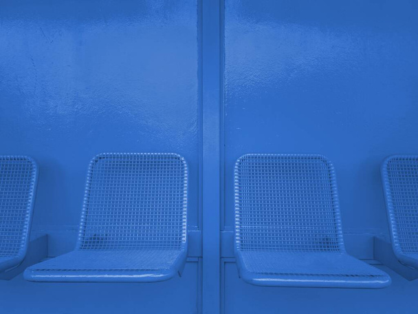 Horizontal shot of empty chairs attached to a blue metal wall during daytime - Foto, Imagem