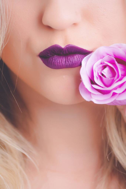 A closeup shot of a female wearing purple lipstick with pink rose close to her lips - great for a fashion article - 写真・画像