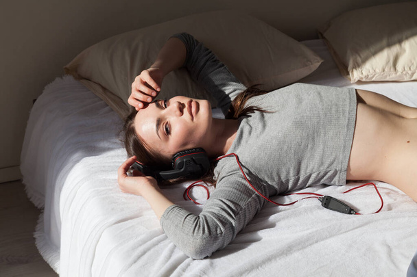 Hermosa mujer escucha música con auriculares en el dormitorio
 - Foto, Imagen