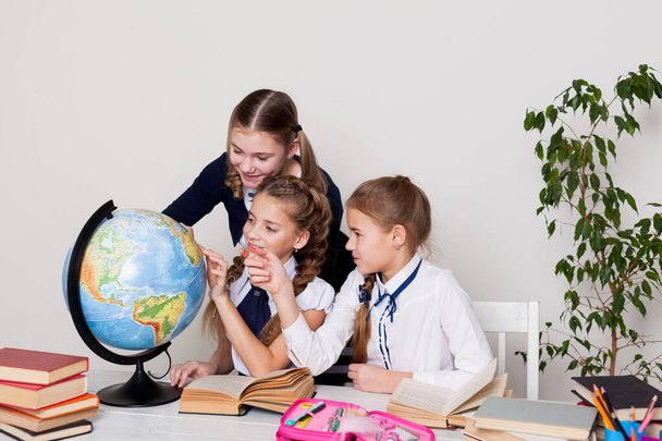 três meninas com livros e um globo na sala de aula na escola
 - Foto, Imagem